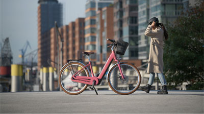 Een vrouw loopt naar een roze Cube Ella Hybrid e-bike in een stad.