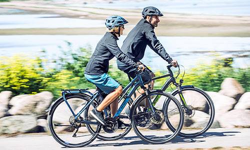 Man en vrouw rijden op trekkingfietsen langs de zee.