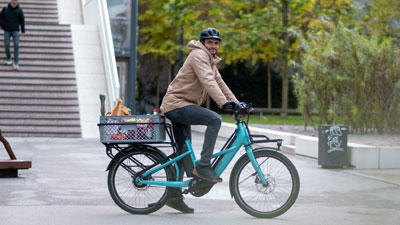 Een fietser rijdt op zijn blauwe Cube Longtail door het stadscentrum. Hij heeft een doos boodschappen op de bagagedrager.