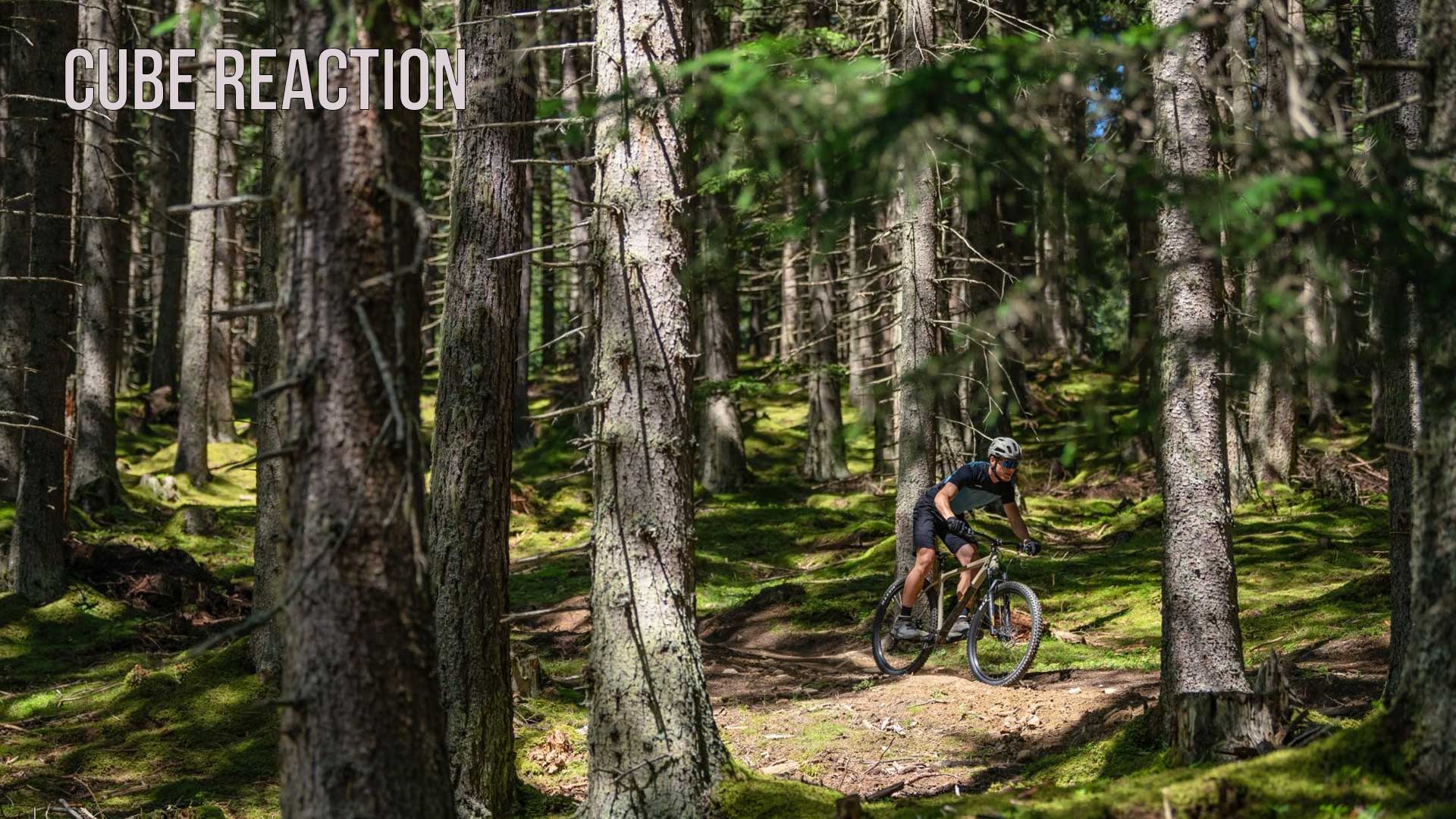 Fietser rijdt op een Cube Reaction hardtail mountainbike door een bos, onderschrift van de foto is Cube Reaction.