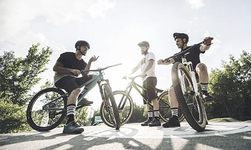 Drie freestyle fietsers staan bij hun fiets en maken een praatje op een zonnige dag.
