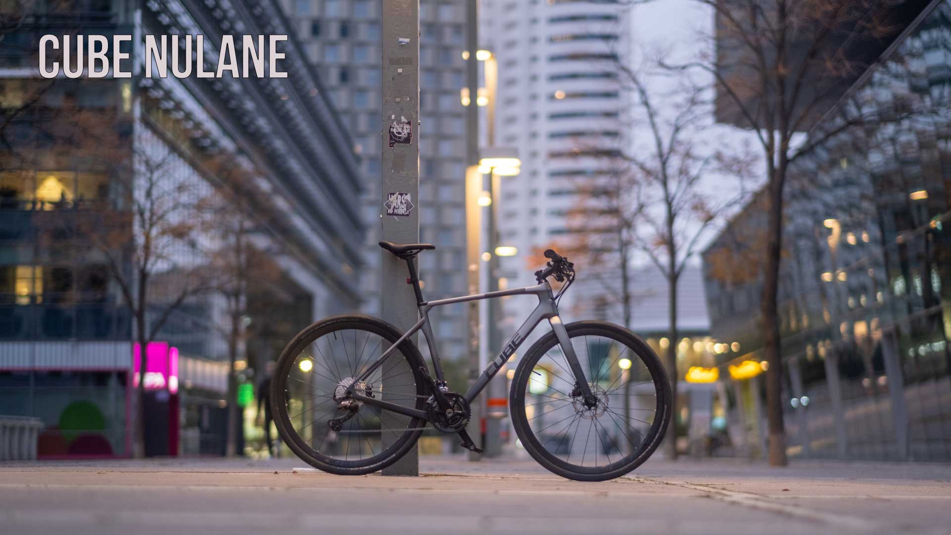 Spandoek met het opschrift Cube Nulane. Een Cube Nulane fitnessfiets leunt tegen een pilaar in het stadscentrum.