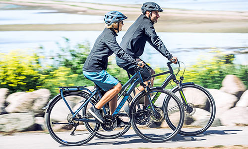 Man en vrouw rijden op trekkingfietsen langs de zee.