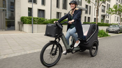 Een vrouw rijdt op een grijze bakfiets door een woonwijk.