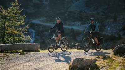 Een stel op een mountainbike op een fietspad, met een berglandschap op de achtergrond.
